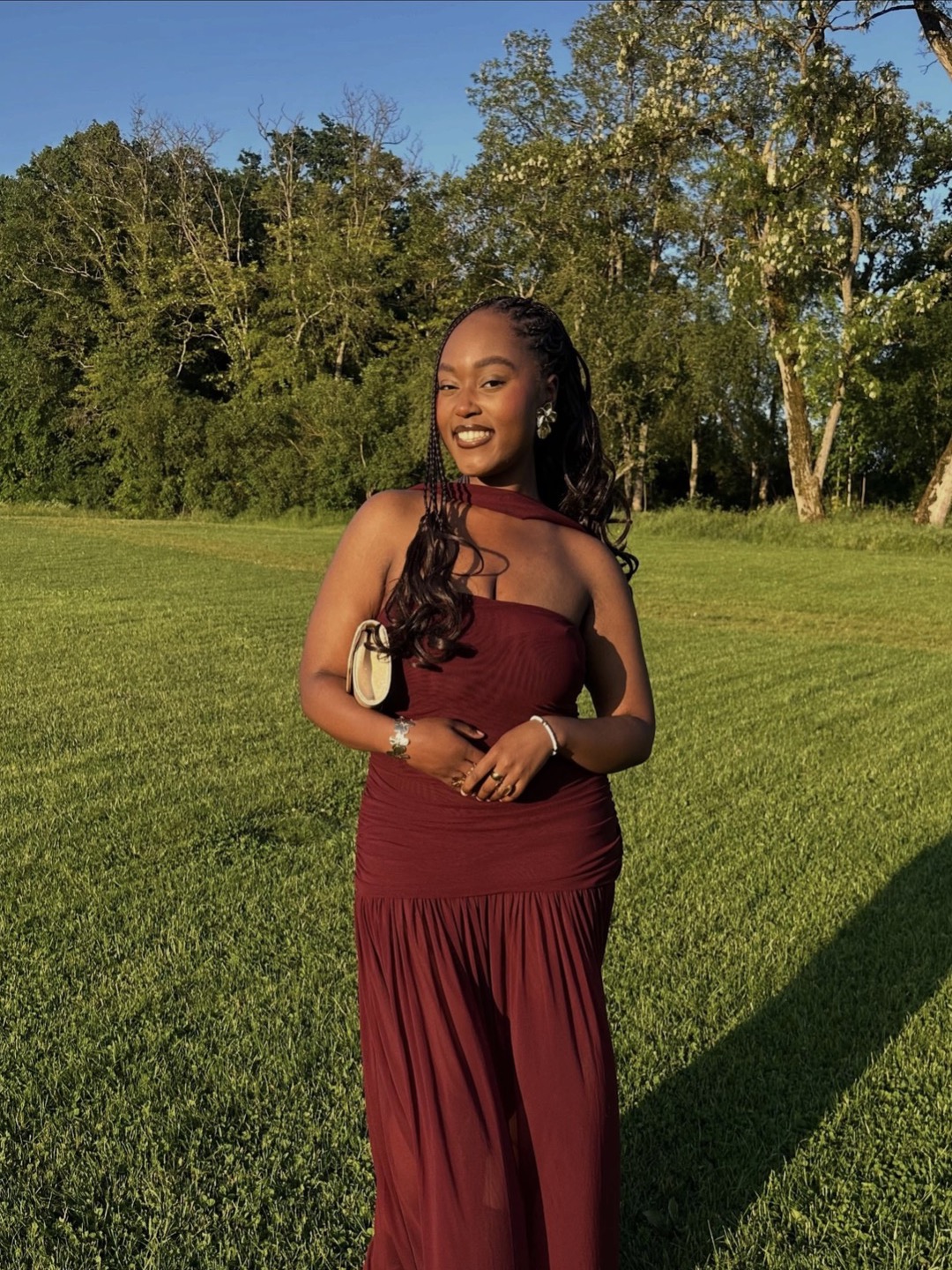 Marie sourit dans un parc, vêtue d'une robe bordeaux
